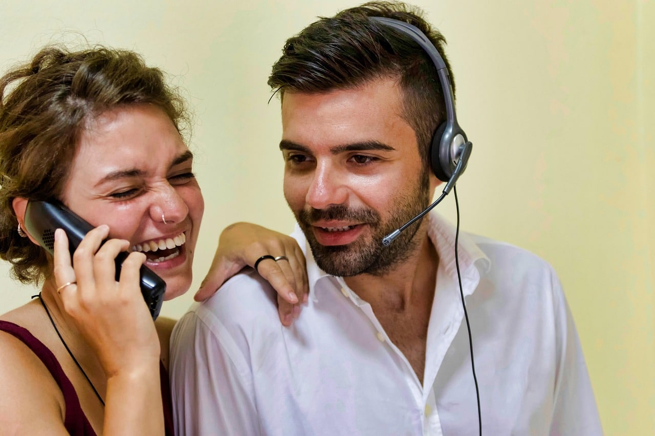 Operatori di call center che collaborano e sorridono durante una telefonata, simbolo di un ambiente di lavoro positivo ed efficace.