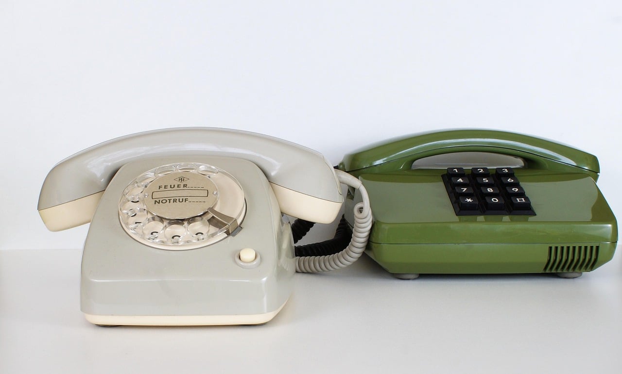 Due telefoni vintage, uno a disco grigio con scritta "Notruf" e uno verde con tastiera a toni,